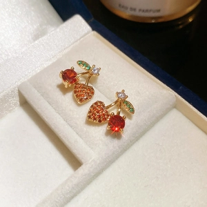 Detailed macro of cherry-shaped gold earrings with red zircons in white jewelry box