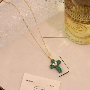 Detail of cross pendant necklace with green malachite texture and small heart accent