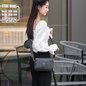 Detail of black chevron quilted crossbody bag with small round coin purse on shoulder strap