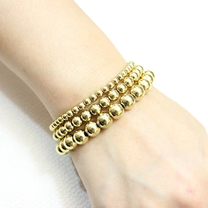Close-up of 18K gold-plated beaded bracelets in four sizes on a woman's wrist