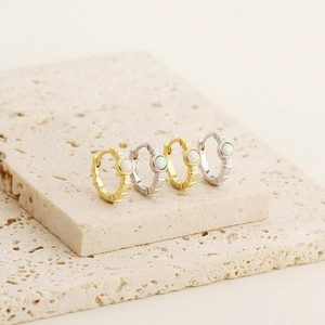 Detailed view of S925 silver and gold opal hoop earrings on a textured stone base