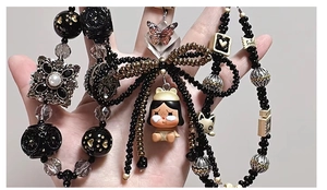 Detailed view of a Y2K phone strap with black beads and a crybaby character pendant