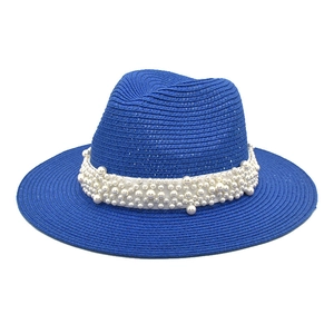 Detail of royal blue straw sun hat with decorative white ribbon and faux pearl accents