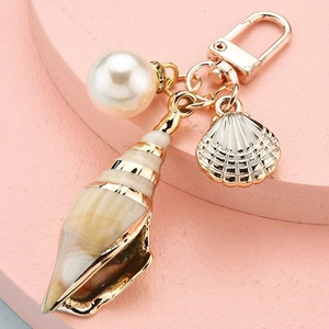 Cute cartoon conch seashell keychain with white pearl and golden accents on pink stand