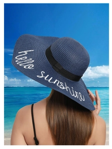 Detail of navy blue straw hat with black ribbon and white hello sunshine embroidery
