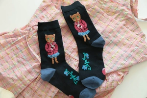 Detail of black cotton socks featuring an embroidered cat holding a rabbit and blue flowers