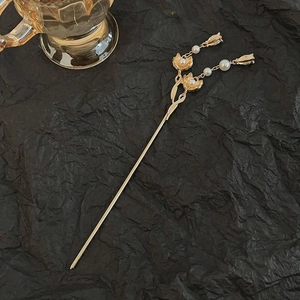 Detail view of golden hair pin with floral motifs and elegant pearls on black paper