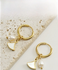 Detail shot of pearl and shell drop earrings on a textured stone tray