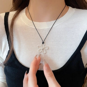 Détail du pendentif fleur argentée ajourée sur cordon noir porté par un mannequin