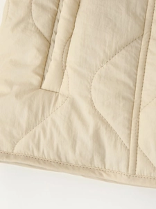 Detailed view of beige diamond-quilted jacket featuring high-quality stitching and piping