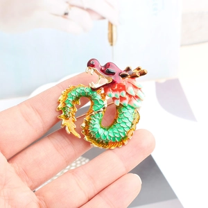 Hand-held view showing the detailed enamel dragon brooch in red and green colors