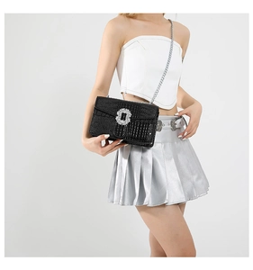 Detail of black textured crossbody bag with sparkling rhinestone buckle and silver chain
