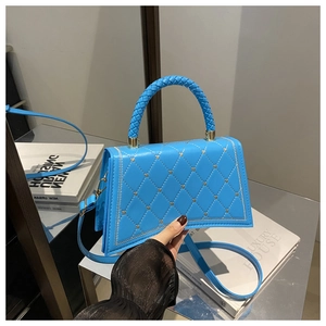 Detail of blue quilted handbag with silver heart accents and woven handle on display