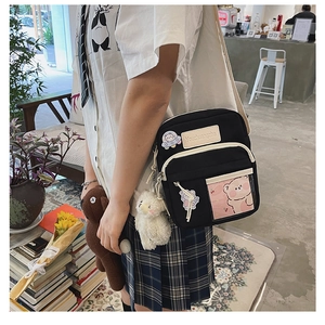 Gros plan sur un sac bandoulière en toile noire avec badges et pendentifs en peluche