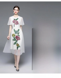 Détail d'une robe en mesh blanc avec broderie florale 3D colorée et motifs à pois