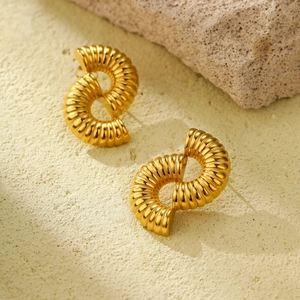 Goldene hohle Spiralohrringe auf sandigem Grund mit Akzenten aus Naturstein