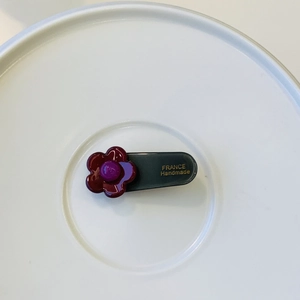 Detail of flower hair clip with deep wine red petals and gold handmade inscription