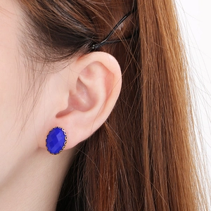 Detail of oval blue glass stud earring with gold wavy bezel setting on a model