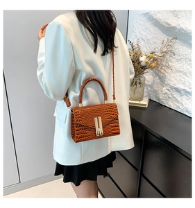Brown crocodile embossed leather crossbody bag worn by a model in a white blazer