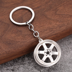 Detail of silver 6-spoke car wheel hub keychain on a walnut wood and grey textured surface