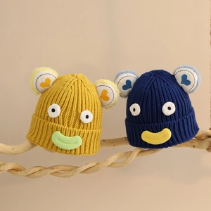 Détail de bonnets tricotés pour enfants avec yeux 3D et lèvres sur branche de bois