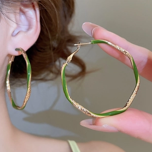 Close-up of golden twisted hoop earrings with green enamel stripes and vintage design