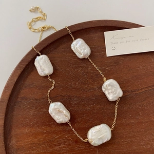 Detailed view of baroque freshwater pearls on a gold chain over a dark wooden tray