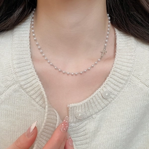 Close-up of elegant pearl necklace with silver cross pendant on female neck
