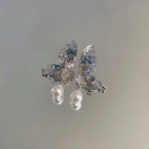 Macro shot of silver butterfly drop earrings with blue crystals and glossy white pearls