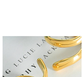 Close-up of golden wavy organic ring with high-polished finish on white printed paper