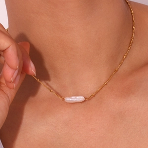 Detailed view of irregular baroque pearl pendant on a thin gold chain worn by a model