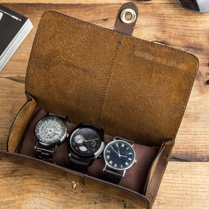 Vintage brown leather travel watch case with three slots and buckle on a wooden desk