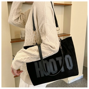 Detail of a large black corduroy tote bag with HOOTO letter patch and metal chain strap
