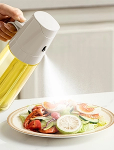 Macro shot of glass oil sprayer misting on fresh salad for healthy meal preparation