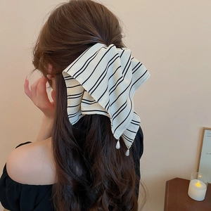Détail d'une pince à cheveux nœud rayé avec pendentif perle sur cheveux ondulés