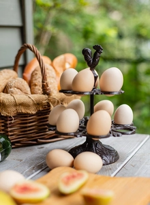 Détail du porte-œufs vintage en fonte avec poignée de coq dans un décor de cuisine rustique