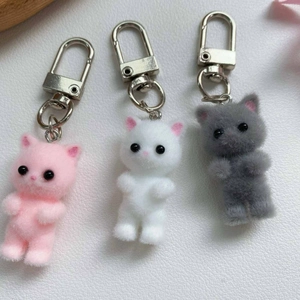 Close-up of three cute flocked cat keychains in pink white and grey with metal clasps