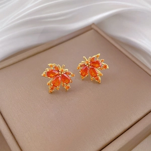 Detailed close-up of maple leaf earrings with sparkling orange gemstones and gold finish