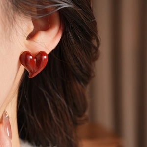 Close-up of a model wearing deep red heart-shaped earrings with a glossy gold finish