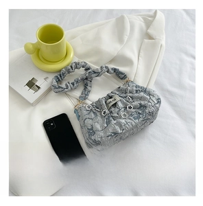 Detail of grey pleated cloud bag with metal flower chain and fabric texture on white suit