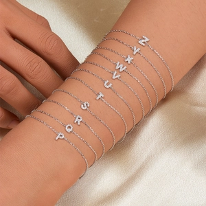 Macro detail of 925 silver alphabet bracelets with zircon inlay on silk background