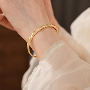 Macro detail of gold-plated bamboo bangle with sparkling zircon inlay on woman's wrist