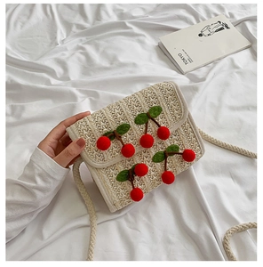 Detail view of woven straw crossbody bag featuring 3D red cherry accents and rope strap