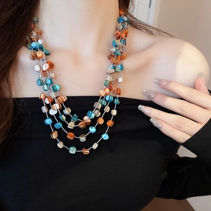 Detail of multilayer shell bead necklace in orange and blue tones on model neck