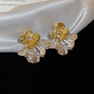 Detail von zweifarbigen Goldblumen- und Silberblatt-Ohrringen auf weißem Seidenstoff