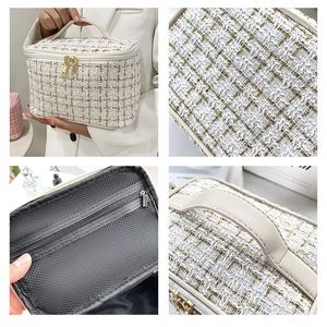 Detail view of white tweed cosmetic bag with golden zippers, mesh pocket, and hand strap