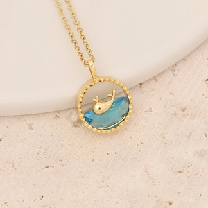 Detailed close-up of a golden whale tail necklace with blue gemstone ocean wave pendant