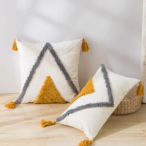 Detail of bohemian cushion covers with yellow tassels and grey tufted triangle patterns