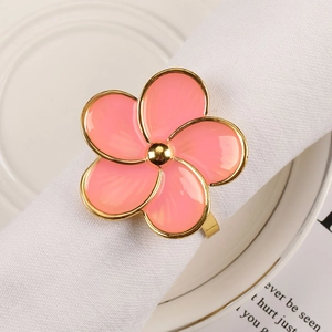 Close-up of pink enamel five-petal flower napkin ring with gold edges on white linen