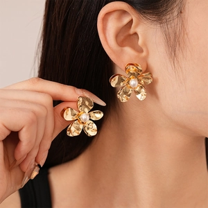Detailed close-up of a gold petal flower earring with an elegant pearl center on a model